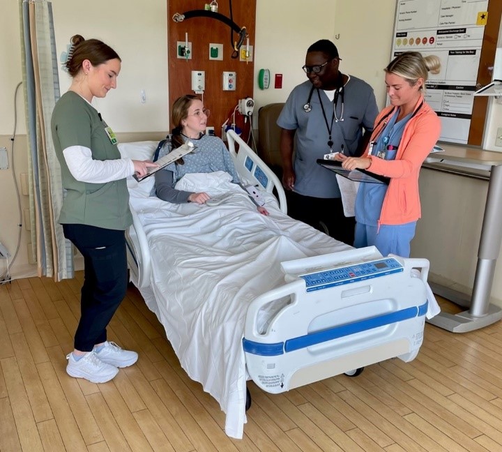 Three nurses meet at a patient's bedside to go over her care