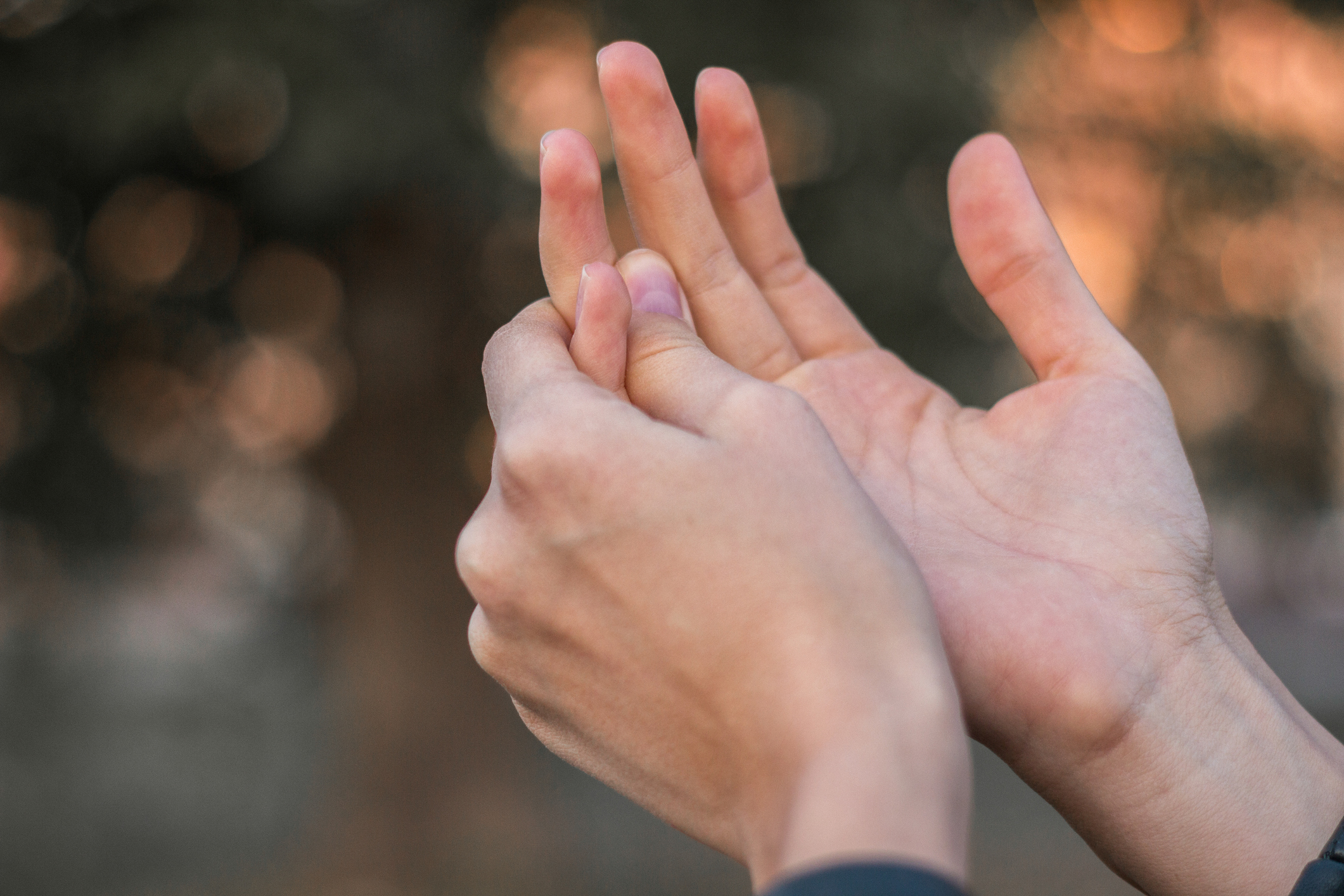 A close up view of two hands as a person holds one of their fingers due to finger pain.