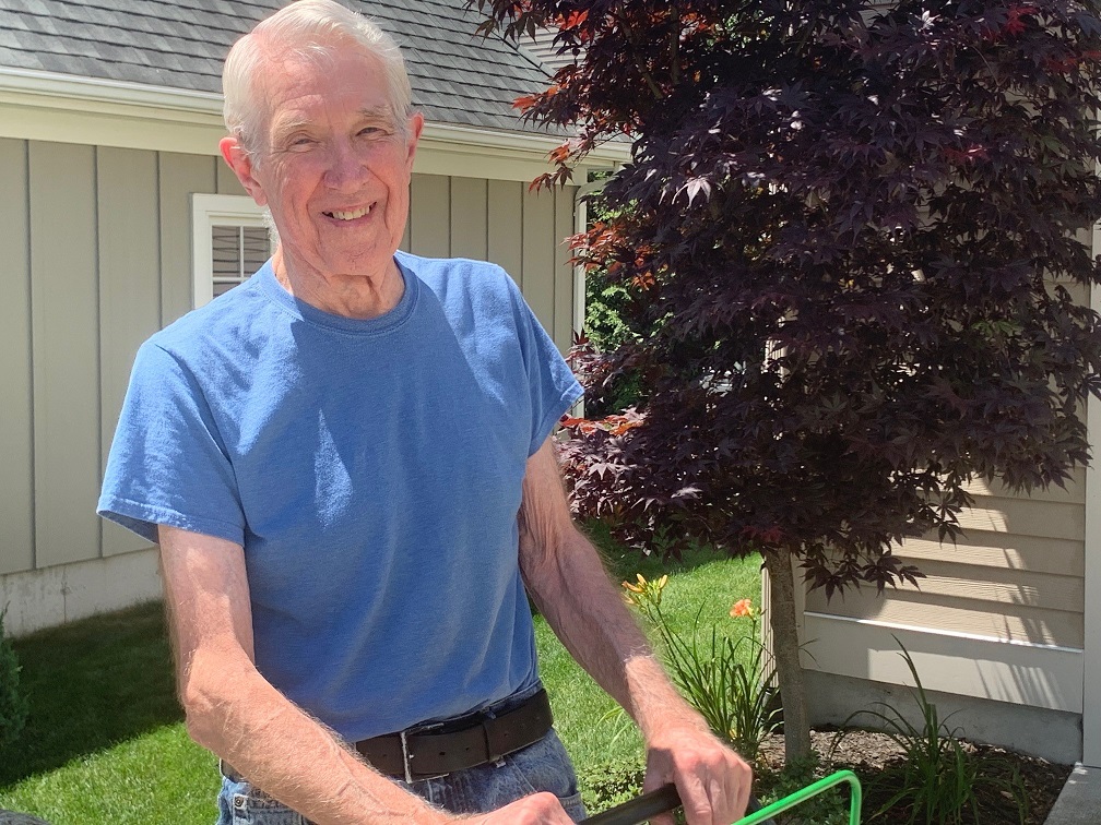 An elderly man smiling while pushing a lawn mower
