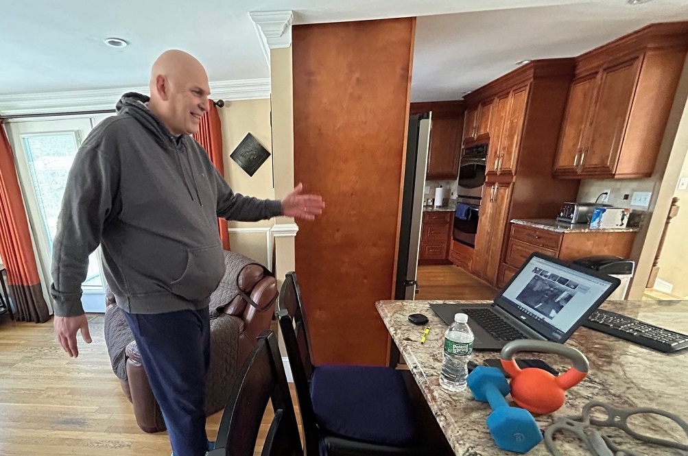 A man exercising in his kitchen to a virtual fitness class on a laptop