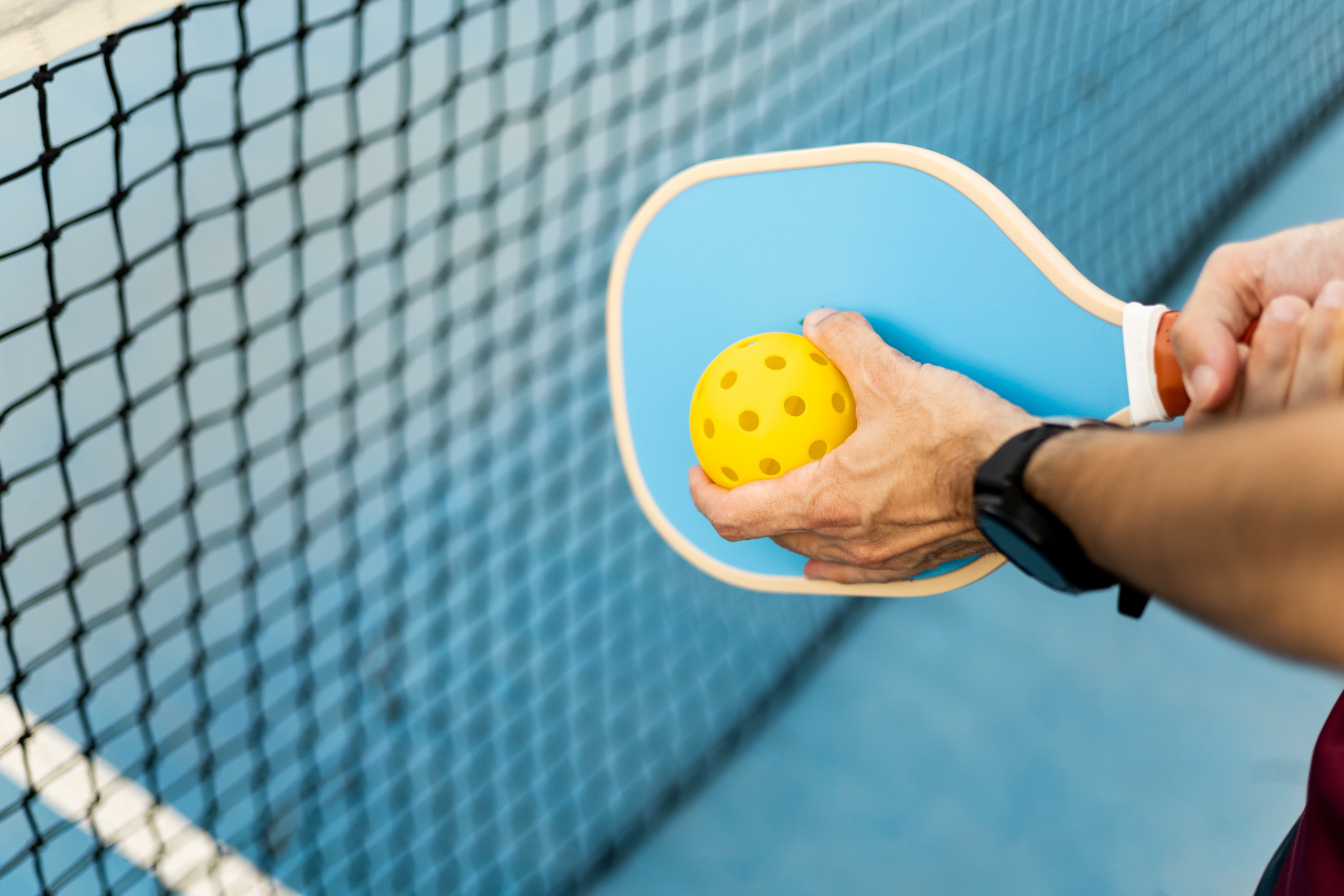A view of a person holding a yellow pickleball in front of a blue pickleball paddle.