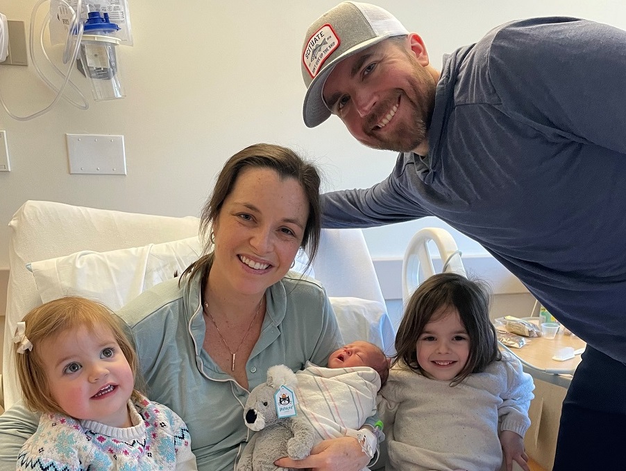 A woman and a man in a hospital room with two little girls and a baby