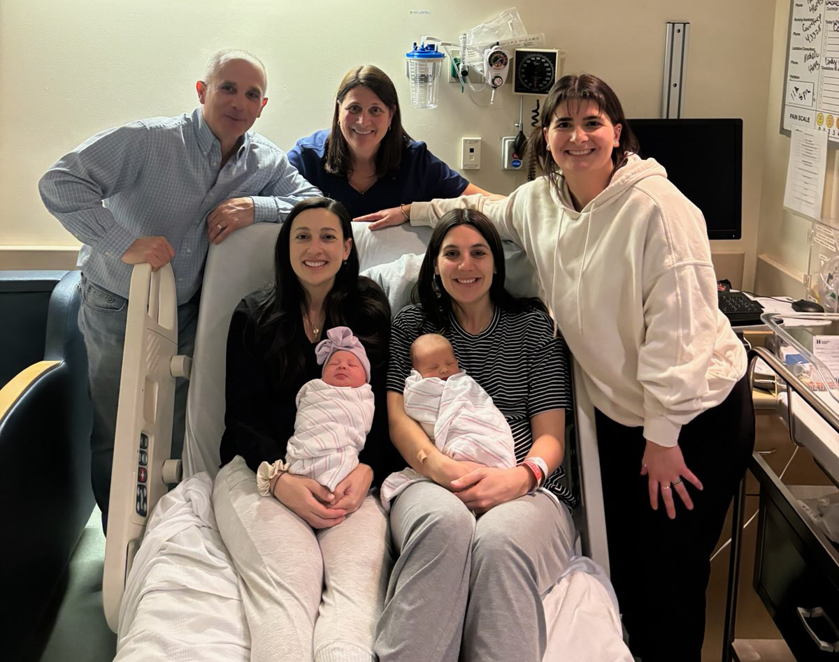 The Miceli Family, with the new moms and babies sitting on a hospital bed, pose for a photo.