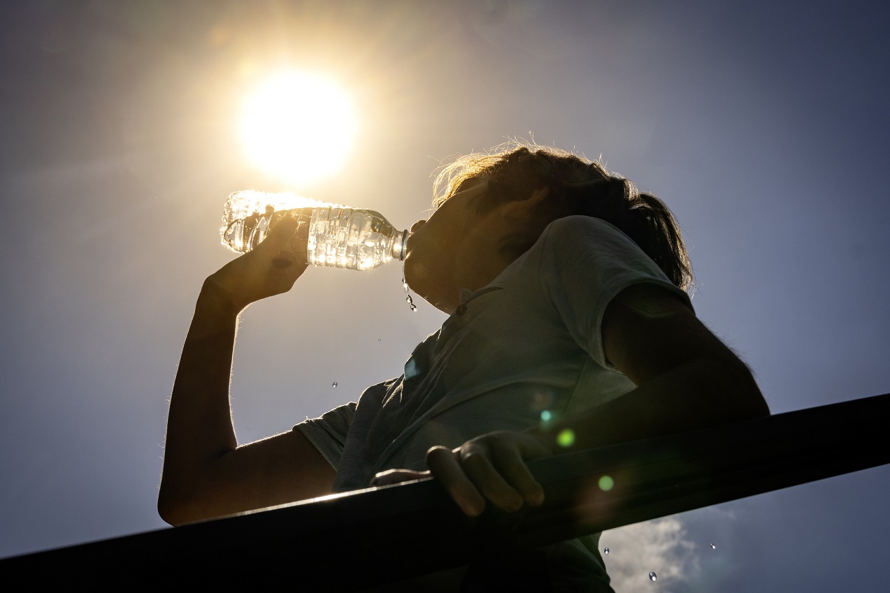 A woman drinking a bottle of water in the hot sun