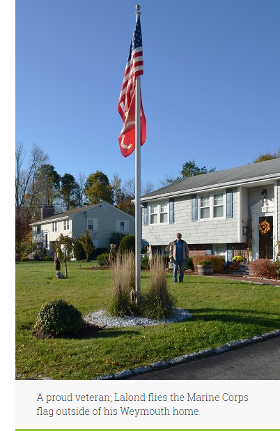 Richard Lalond stands behind his flag pole, looking at the American and Marine Corps flags