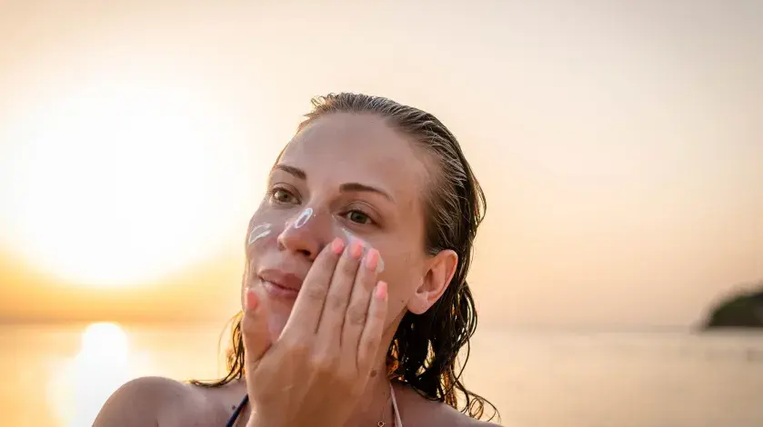 A woman applies sunscreen to her face