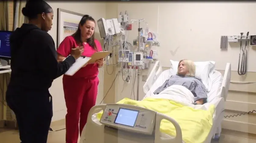 Two female nurses stand by a female patient's bedside and go over her care plan 