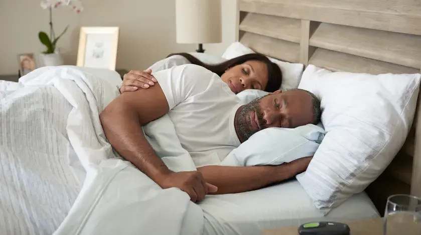 A man lies sleeping on his side in bed with the remote for his Inspire Therapy device on the nightstand next to him.