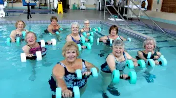 Older ladies holding weights and smiling in a pool class