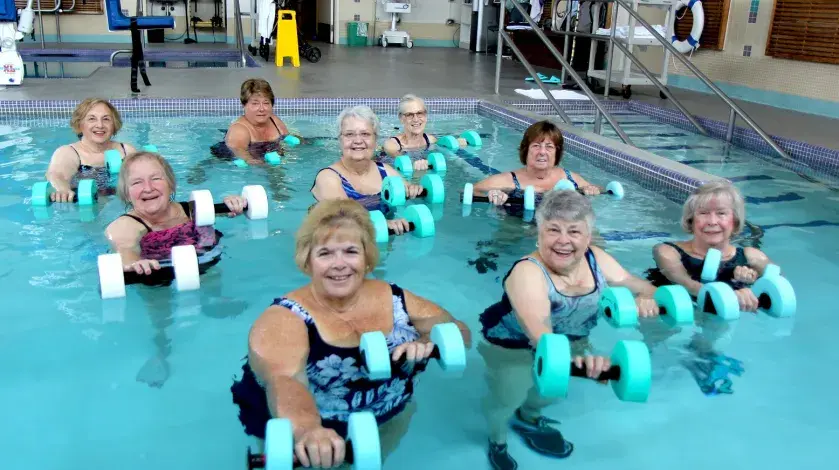 Older ladies holding weights and smiling in a pool class