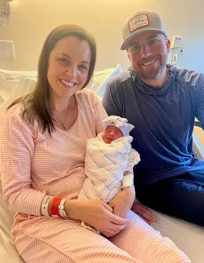 A woman holding a newborn on a bed with her husband