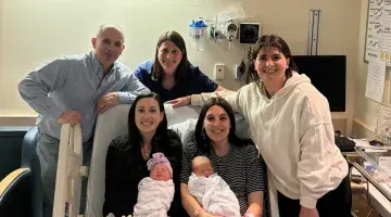 The Miceli Family, with the new moms and babies sitting on a hospital bed, pose for a photo.