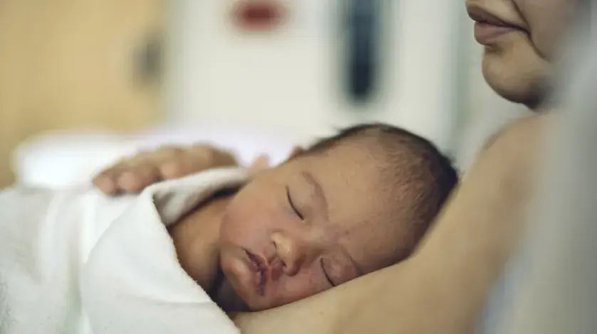 Close up view of a sleeping newborn resting its head on its mother's chest as part of skin-to-skin contact during the Golden Hour.