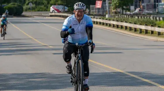 A Team South Shore Health PMC rider gives a thumbs up to the camera as he rides in the 2025 event.