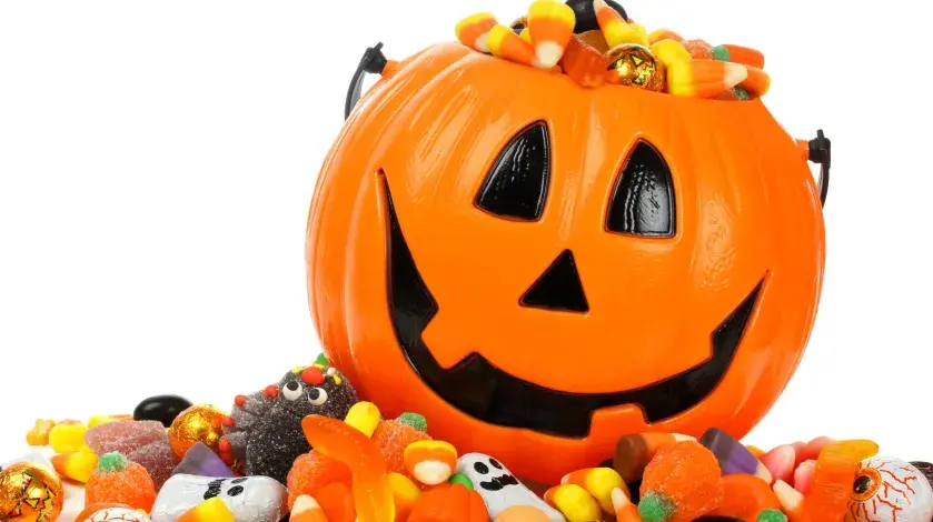 A plastic jack-o-lantern pumpkin filled with candy sits atop a pile of additional candies.