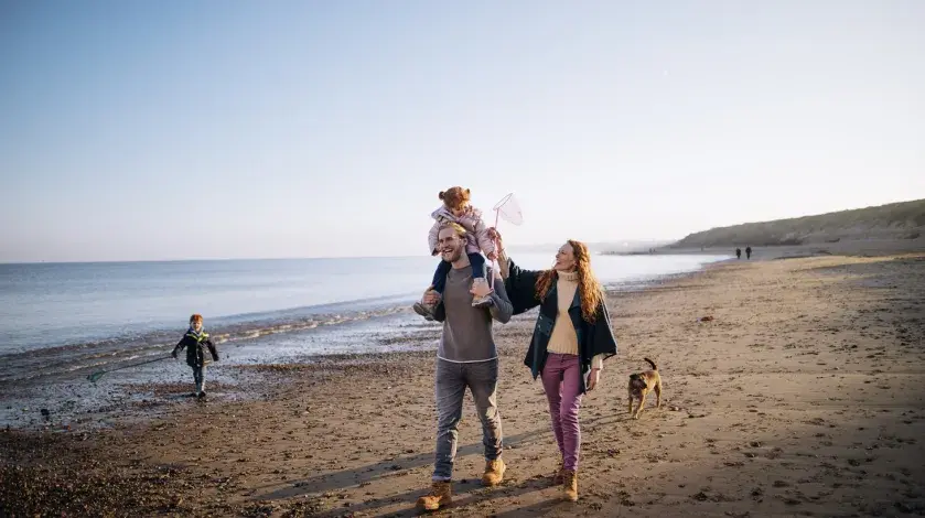 A couple with two young kids and a dog walks near the ocean on the beach