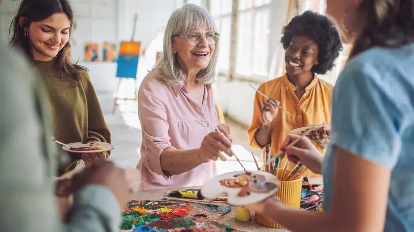 A group of women smile as they paint together at a painting class