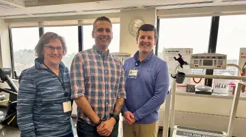 A male patient stands near a treadmill between a female nurse and male exercise physiologist